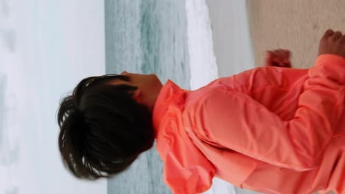 Chubby female running along empty beach near seashore. Vertical video