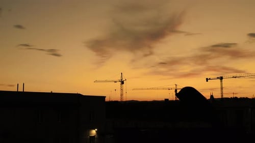 Construction Cranes Silhouetted Against Vivid Cityscape at Sunset
