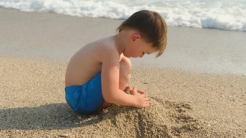 Little Child Building Sand Castle Sitting On Beach In Summer