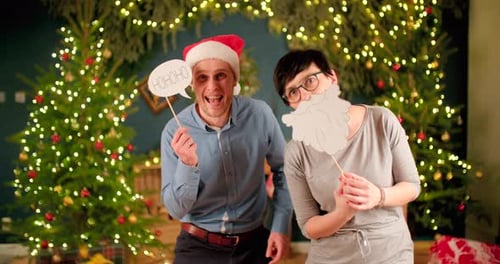 Man holding funny Christmas sign up while woman has a beard shaped sign in front of her face