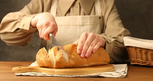 Frau schneidet frischen Brotlaib am Holztisch, Nahaufnahme