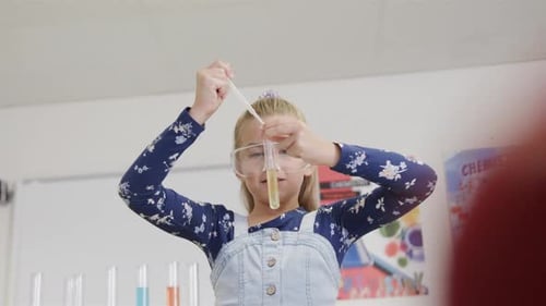 Focused caucasian schoolgirl doing experiment in elementary school chemistry class, slow motion