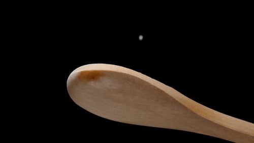 Salt Falls Down from a Wooden Spoon. The Chef Salts the Dish. Slow-Motion, Macro, View from Below.