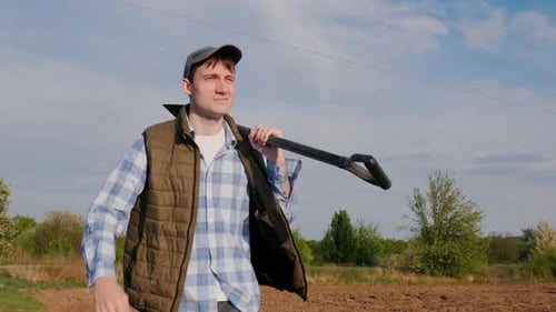 Farmer Walking Across Field with Shovel on Shoulder