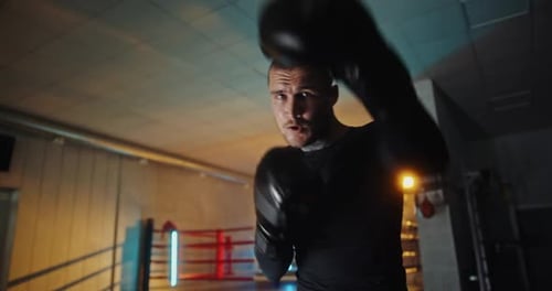 Konzentriertes Boxertraining in Handschuhen mit der Kamera im dunklen Fitnessstudio