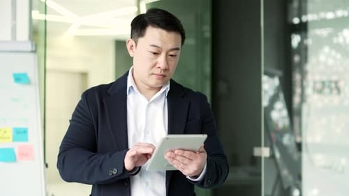 Serious asian businessman is using digital tablet standing in business office.