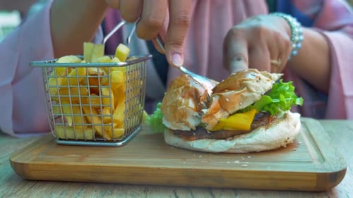 Cutting a burger with cheese lettuce and french fries