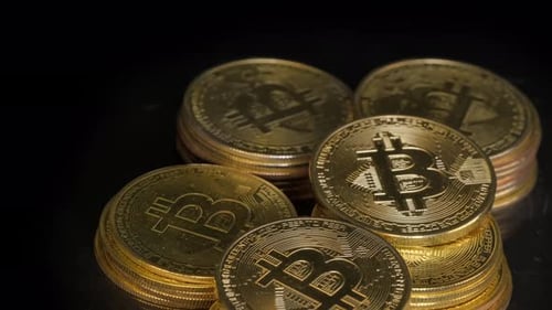 Un montón de monedas metálicas de Bitcoin (BTC) colocadas en pilas giran sobre un fondo negro.