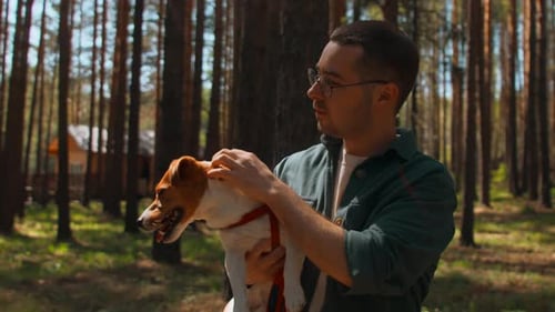 Man Holds and Pets Dog in Sunny Forest