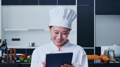 Close Up Of Asian Woman Chef Using A Tablet In Home Kitchen