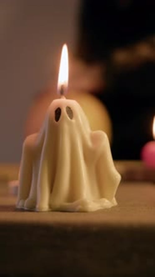 Halloween Ghost Candle Burns Brightly in Foreground While Blurred Background Reveals Pumpkin Being