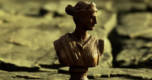Sculpture of a Classical Figure on a Rocky Surface During Golden Hour