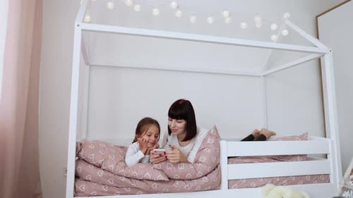 Woman and Child Sharing Smartphone in House Bed