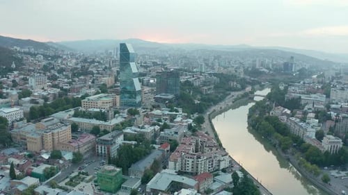 Aerial view of downtown Tbilisi, Georgia at sunset with mountains in the background. Camera approach