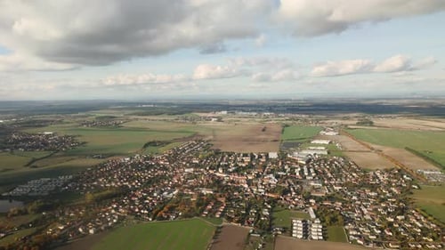 Flying in blue sky beneath cumulus clouds over green fields and houses on Prague's outskirts