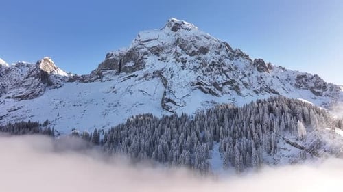 Aerial view of a snow-capped mountain peak of Fronalpstock piercing a sea of fog in Glarus.