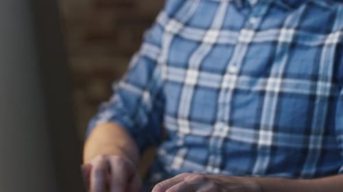 Young man in glasses is sitting in front of a monitor in a loft and working.