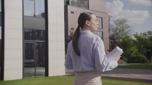 Businesswoman Walking Near Business Center and Holding Documents in Her Hands