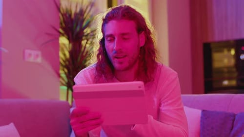 Man video calling using tablet on sofa at home