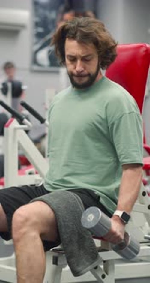 Vertical Footage of a Bearded Man Training Biceps with Dumbbells During an Intense Gym Workout