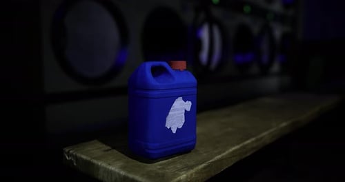 Container with White Emblem Sits on Wooden Table in a Dim Laundromat