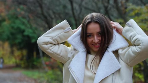 Cheerful positive lady puts on warm jacket walking in the park.