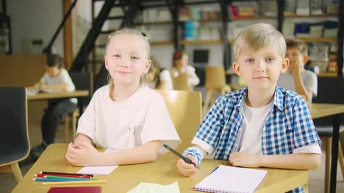 Two Happy Elementary School Classmates a Boy and a Girl Sitting at a School Desk Looking at the