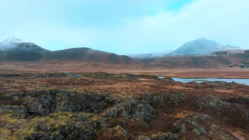 Lava field beneath Iceland's rugged mountains and volcanic cones - sliding drone reveal