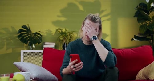 Man looks at phone and puts hand on face