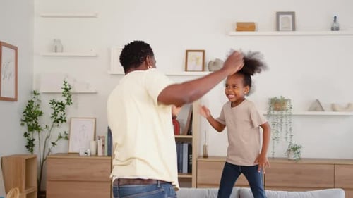 active father and his little daughter share laughter as they jump and dance on the sofa.