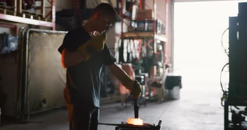 Professional blacksmith shapes red hot metal inside dark workshop
