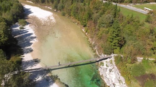вид с воздуха на человека, идущего по веревочному мосту через реку Соча в Словении