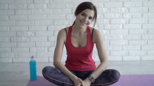 Woman Smiles While Sitting Cross-Legged on Yoga Mat