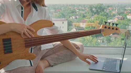 Young Woman Plays Bass Guitar by Window