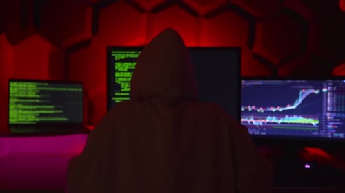 Anonymous hacker writing code in a dark red room.