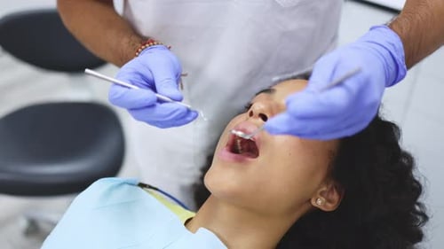 Nahaufnahme eines nicht wiederzuerkennenden Zahnarztes mit Maske und Handschuhen, der einen Untersuchungsspiegel trägt und überprüft
