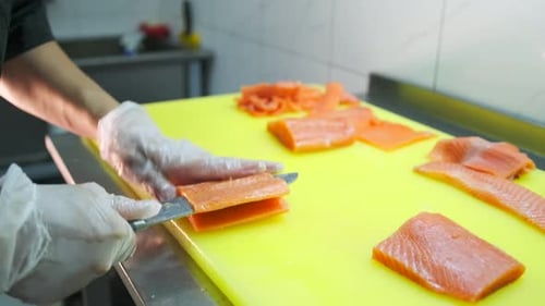 The hands chef cuts with knife the salmon at the professional kitchen, prepares raw red fish