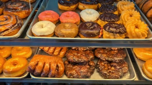 Nahaufnahme eines Displays voller süßer Snacks, Donuts, Gebäck unter Ladenlichtern.