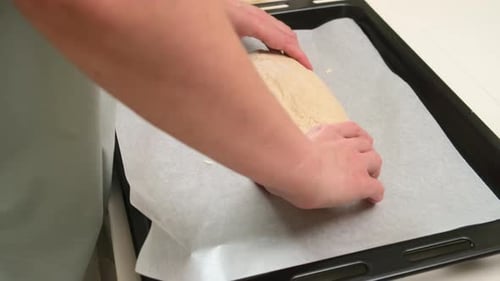 Eine Person formt rohen Brotteig auf einem mit Backpapier ausgelegten Backblech und bereitet ihn für das Backen zu Hause vor