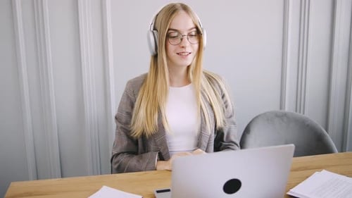 Professional Woman Engaged in Virtual Meeting at Home Office with Headphones and Laptop During