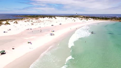 Idyllic clear blue water of sandy Moonlight Beach with beachgoers and lighthouse