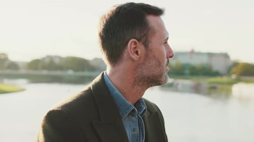 Close up, man looks around while sitting on the embankment on the background of the river