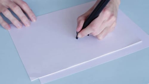 Person With Black Pentel Pen Draws A Zigzag Pattern In White Paper. High Angle
