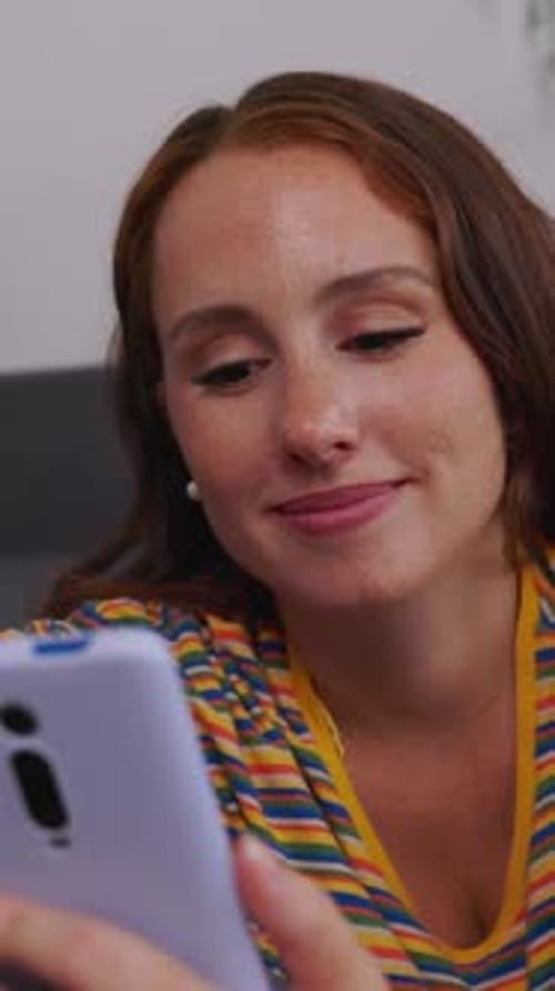 Young Adult Woman Relaxing on Sofa Using Mobile Phone at Home