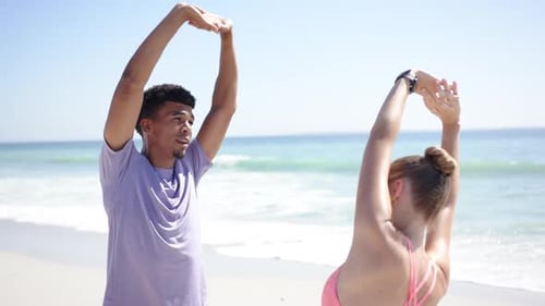Junger biracialer Mann und kaukasische Frau strecken sich an einem sonnigen Strand