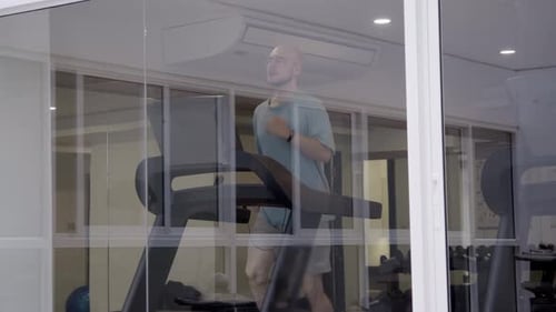 Outside Looking in Shot Captures Gym Member Jogging on Treadmill Through Window Panels Glass