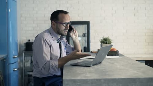 Angry Businessman with Laptop Talking on Cellphone at Home 30s