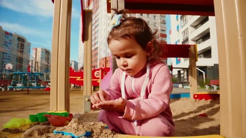 A Young Child in a Pink Outfit Engaged in Play with Sand in a Playground Surrounded By Colorful Toys