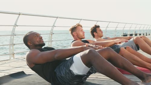 Athletic Men Perform Abdominal Exercises on Seashore