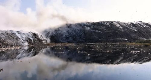 Landfill Polluted and Smoking Next to Reflective Water